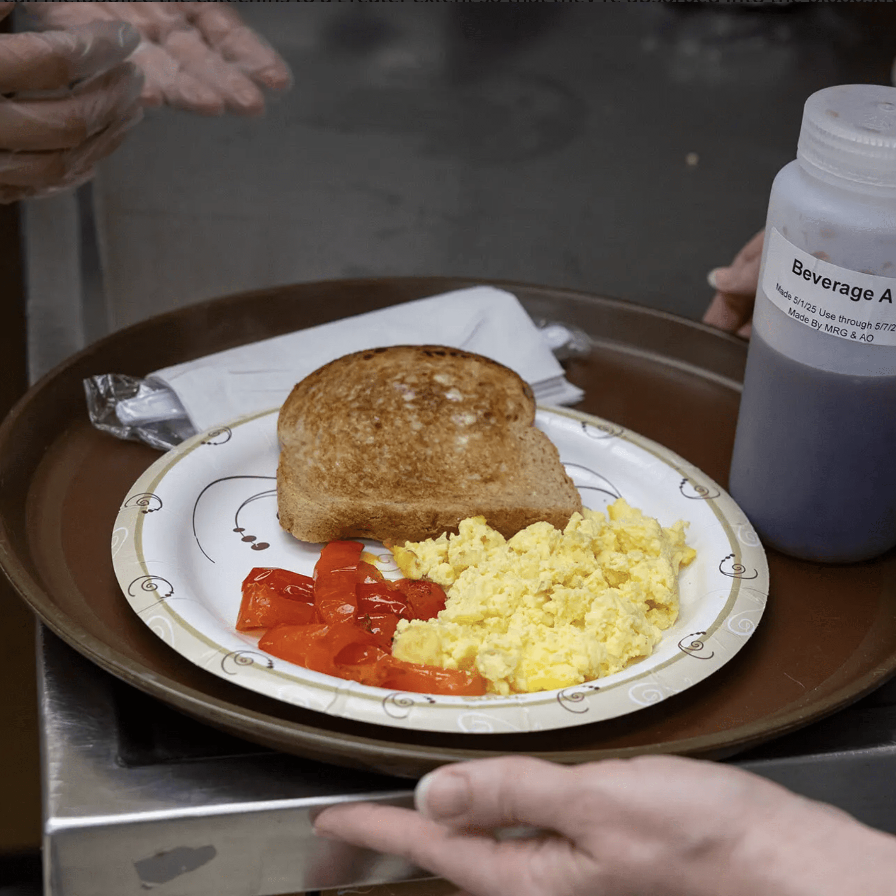 A paper plate with a slice of bread, scrambled eggs, and tomatoes