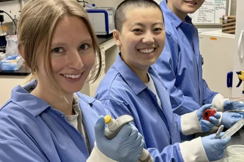 ThreeStudent researchers in a lab, wearing lab coats posing for a photo